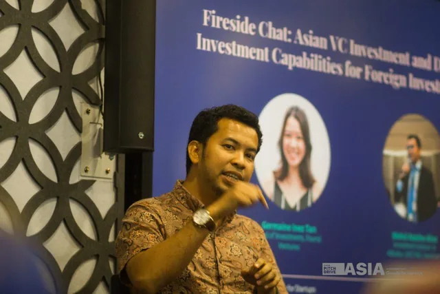 Mohd Atasha speaking during a panel, gesturing, in front of an event backdrop listing the session and its speakers